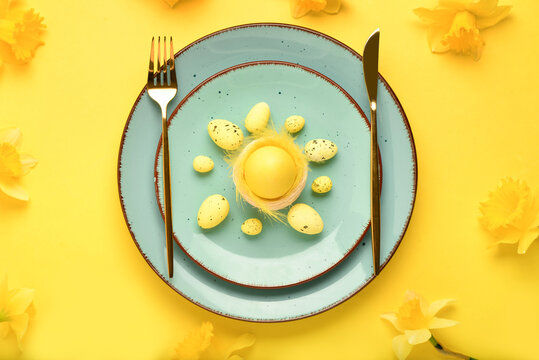 Beautiful festive table setting with painted Easter eggs and narcissus flowers on yellow background