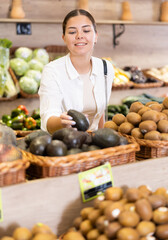 Delighted young woman purchaser choosing ripe avocados at the counter in grocery store