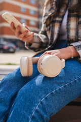 Close up of wireless headphones on girls lap while she is using phone to send messages or listen to music
