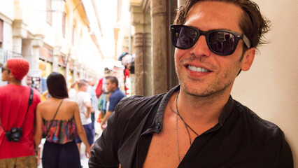 smiling caucasian hispanic tourist with sunglasses and open black shirt at handicraft market in...