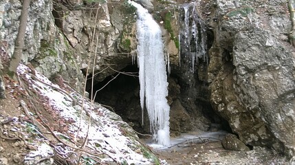  there is a waterfall that has frozen water coming out of the side of a rock formation with snow on the ground.