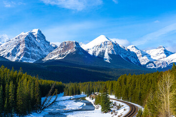 Canadian Rockies in the Winter at Morant's Curve in Banff National Park featuring Haddo Peak, Saddle Mountain, Fairview Mountain, Mount Whyte and Mount Niblock. Railway track winds through the valley.