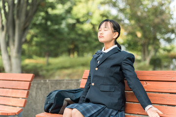 公園のベンチに座り深呼吸する女子中学生・女子高生・高校生
