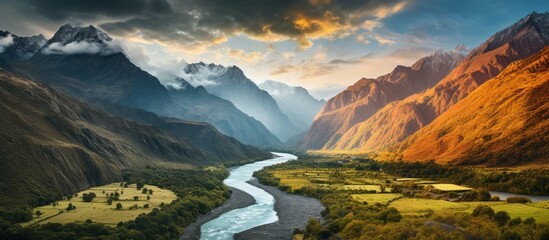 A river meanders through a valley nestled between towering mountains under a sky filled with clouds, creating a breathtaking natural landscape