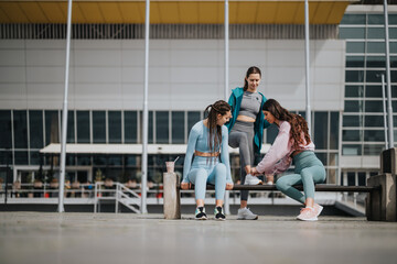 Group of active women in stylish sportswear resting and chatting after a workout session by a modern gym facility.