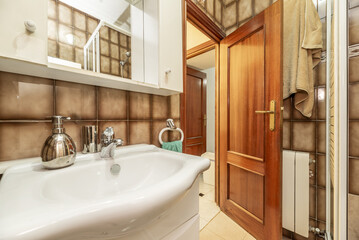An old-fashioned bathroom with dark tiles and light brown floors, white toilets and a cabinet with an integrated mirror.