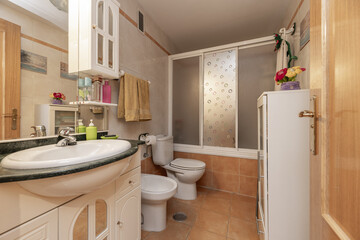 A contemporary bathroom with white tiles and light brown floors, white toilets and a shower cabin with white screens and a cabinet with an integrated mirror