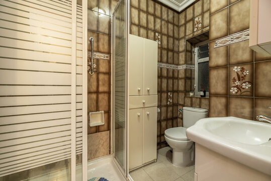 An old-fashioned bathroom with dark tiles, white toilets and a square shower cubicle with screens