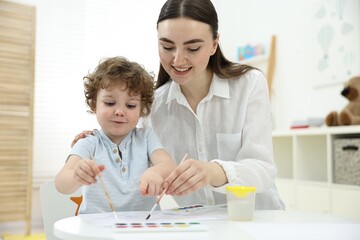 Mother and her little son painting with watercolor at home
