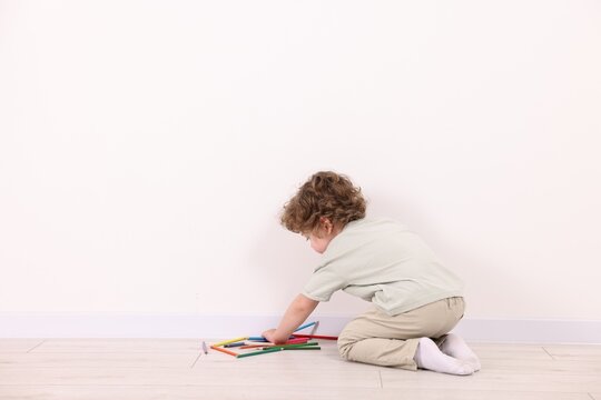 Little boy with colorful pencils near white wall indoors. Space for text