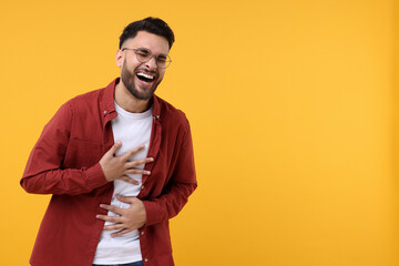 Handsome young man laughing on yellow background, space for text