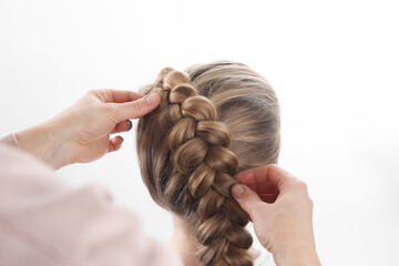 Professional stylist braiding girl's hair on white background, closeup