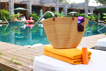Wicker bag with beach accessories on sunbed near outdoor swimming pool. Luxury resort