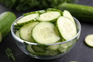 Cut cucumber in glass bowl on dark gray textured table, closeup