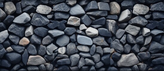 A close up of cobblestone rocks forming a pattern on a wall. These natural building materials are commonly used for flooring and road surfaces - obrazy, fototapety, plakaty