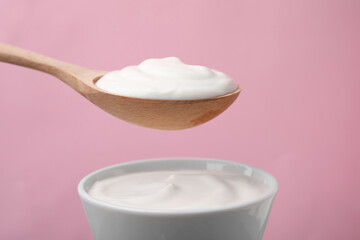 Eating delicious natural yogurt on pink background, closeup