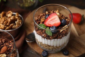 Tasty granola with berries, nuts and yogurt in glass on table, closeup