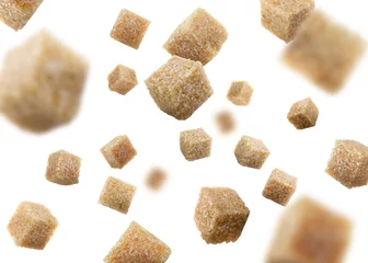  Brown cane sugar cubes falling on white background © New Africa