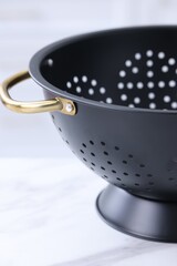 Black colander on white marble table indoors, closeup