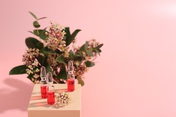 Stylish presentation of skincare ampoules and flowers on pink background, closeup. Space for text