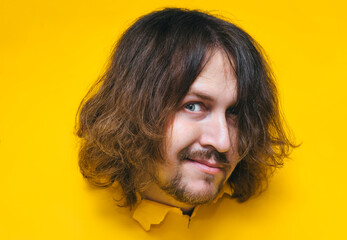 A long-haired, shaggy man with a beard and mustache with a smiling expression on his face looks out...