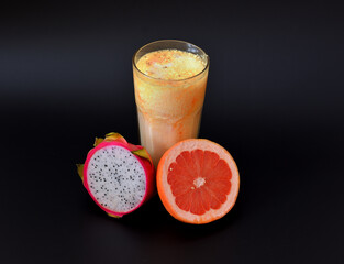 Freshly squeezed grapefruit and pitaya juice in a tall faceted glass on a black background.