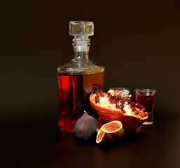 Fig pomegranate liqueur, strong homemade alcohol on a black background, a bottle and two glasses with a drink and slices of ripe fruit.