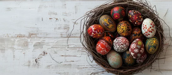 Foto op Canvas Easter eggs adorned with wax-resist dyeing method, known as Pysanky, displayed in a nest on a white wooden surface. The style is a traditional craft popular in Eastern European regions, © Vusal