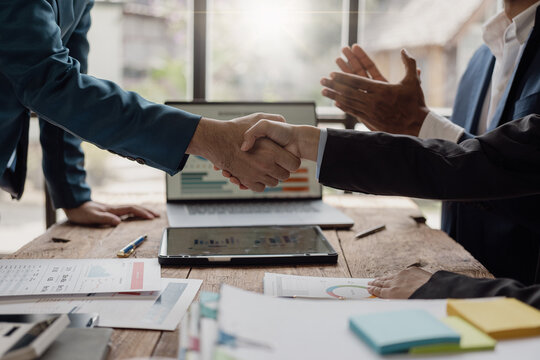 Businessman and investor holding hands as a symbol of friendship and cooperation in business success of cooperation and with documents, financial graphs and laptop on the table. Close-up photo.