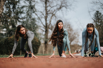 Athletic individuals bent over in ready position on a track, poised for a sprint in an outdoor...