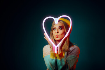 Woman Holding a Neon Heart Making Kissing Face. Cute girlfriend being playful, romantic and flirtatious 