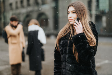 Focused young woman talking on the phone, with blurred colleagues in background on a snowy urban street.