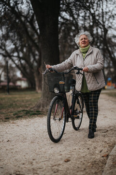 An elderly lady in casual wear stands with her bike, portraying an active lifestyle and leisure in retirement.