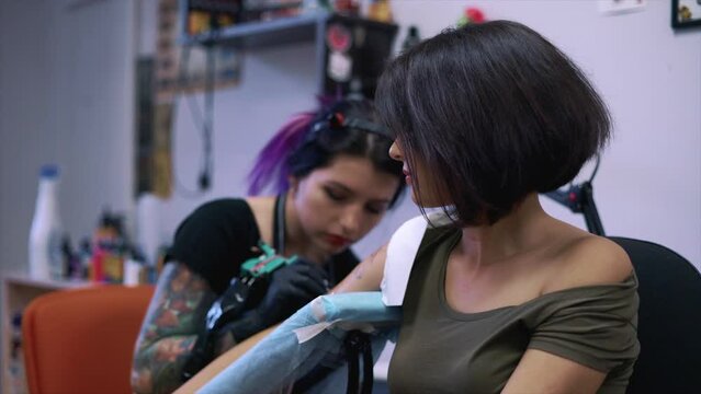 A close-up view of a professional woman tattooist who is tattooing on the leg of a young girl. Hands of a tattooist. Tattooist makes a tattoo.