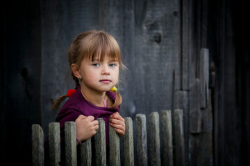 A cute little girl looks out from behind a rustic wooden fence. - 767543318