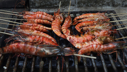 Shrimp are grilled on a steel grate in a tank filled with charcoal.