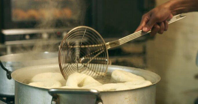 Kitchen, person hands and bagel boiling in a stove pot with chef, food and bread prep in a restaurant. Cafe, water and coffee shop of a professional baker in bistro working with dough and cooking