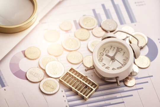 Coins, abacus, and alarm clock placed on financial data reports