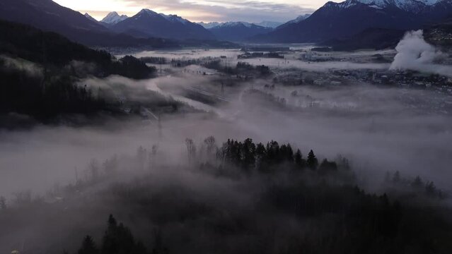 Aerial Drone shot over misty Cityscape at Sunrise Surrounded by Snow Covered Mountains in Frastanz, Vorarlberg, Austria