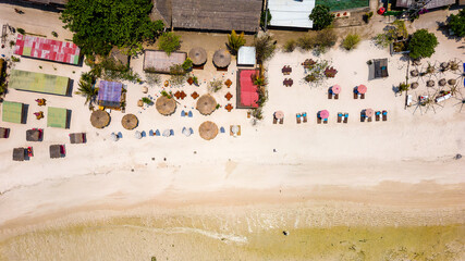 Top down aerial view of various sunshades and resorts along a tropical beach at low tide