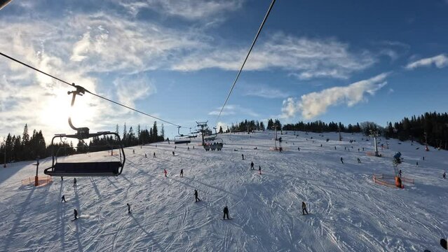 Sunny winter scenery of a crowded ski slope. POV shot from a chairlift.