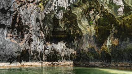 A picturesque karst rock rises above the emerald water. Steep furrowed slopes with caverns. Light...