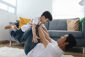 Joyful young man father lying on carpet floor, lifting excited happy little child son at home.