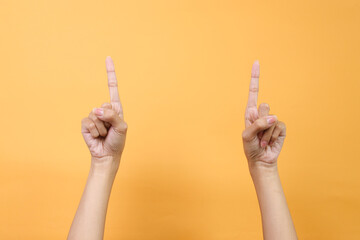 Two hands pointings up to the empty space over yellow background.