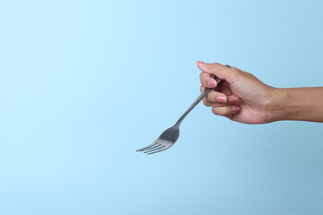 Woman's hand holds a metal fork on a blue background.
