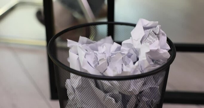 Trash can stands in office filled with discarded paper