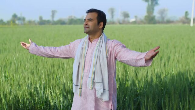 Young village man enjoying the fresh morning breeze of his farms with open arms - desi lifestyle  desi morning. Modern age farmer doing a routine checkup of his farms in the morning - rural area  v...