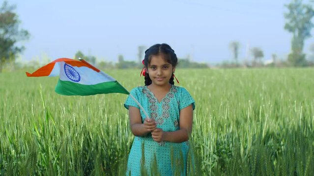 Young village girl proudly swinging the Indian flag in a field - tri color flag  proud citizen  rural lifestyle. Medium shot of a girl child with national flag for republic day celebration - indepe...