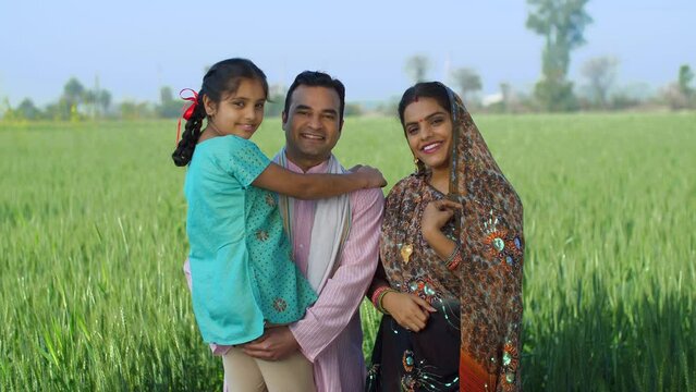 Happy Indian farmer family in fields - rural area  desi lifestyle  village life  nuclear family  girl child. Medium shot of a happy Indian family holding their daughter their arms - field  khet  be...