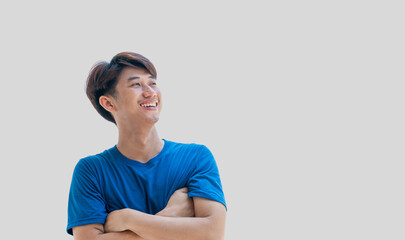 A young Asian man in his 20s wearing a blue t-shirt stands confidently with his arms crossed over his chest, isolated on a gray background. Positive person.